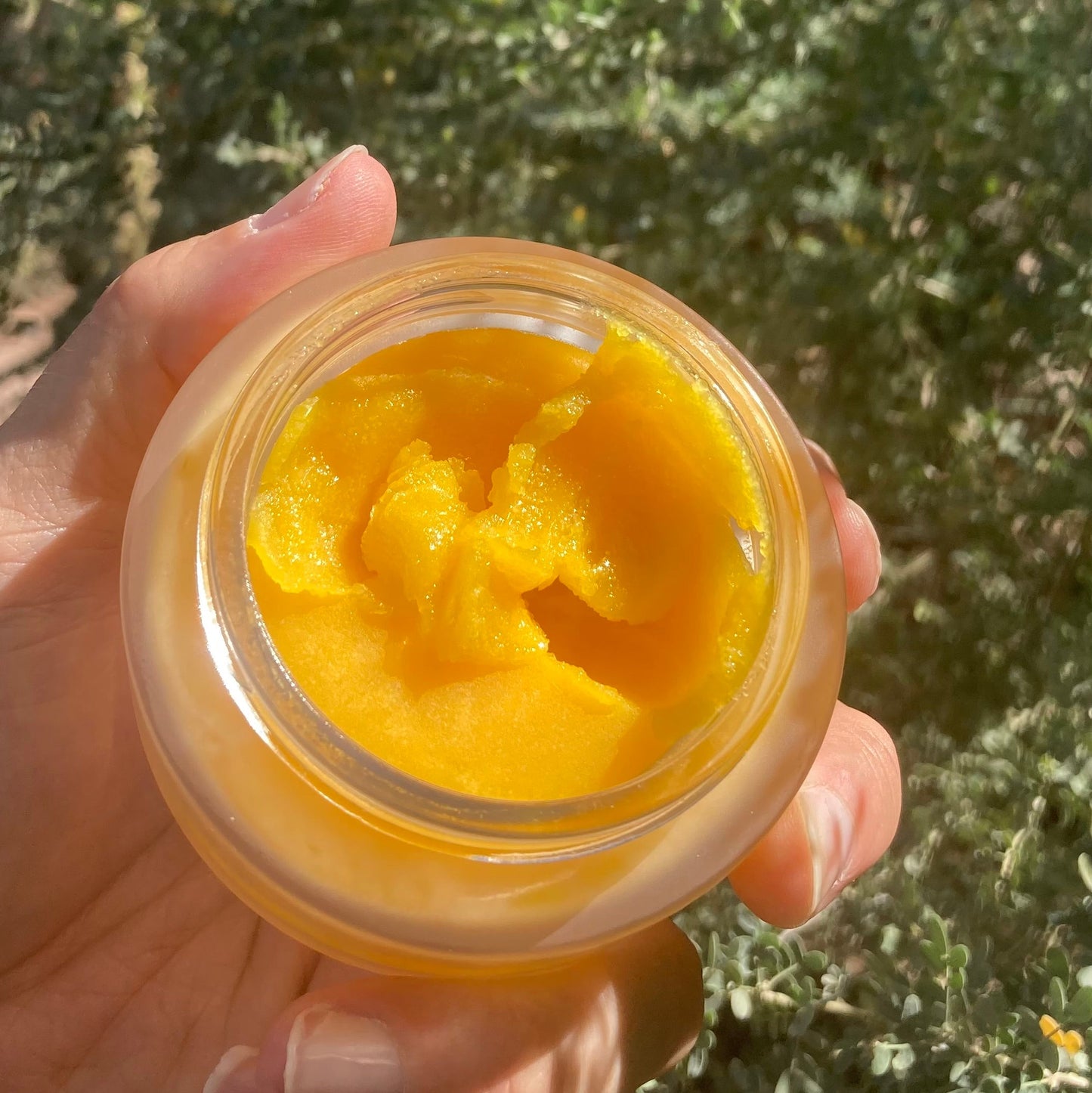 Hand holding a jar of yellow 'Clarifier' cleansing butter against a natural, green background