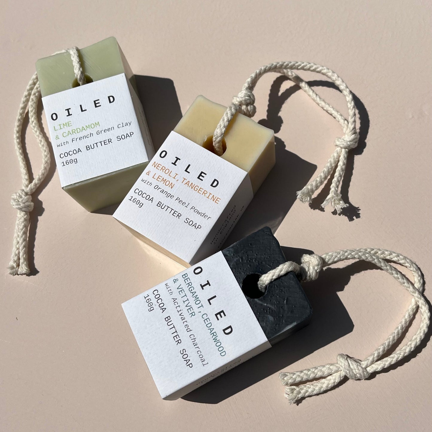 Three bars of 'Oiled' soap on a beige background with ropes attached.