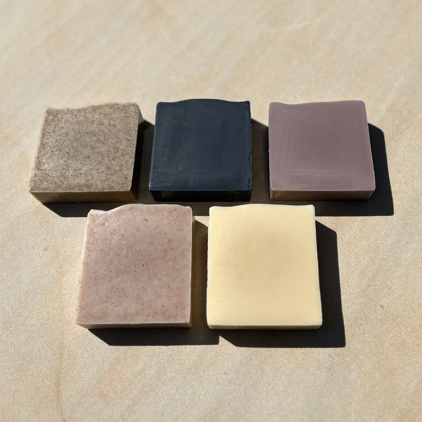 Five square bars of soap in different colours on a beige surface