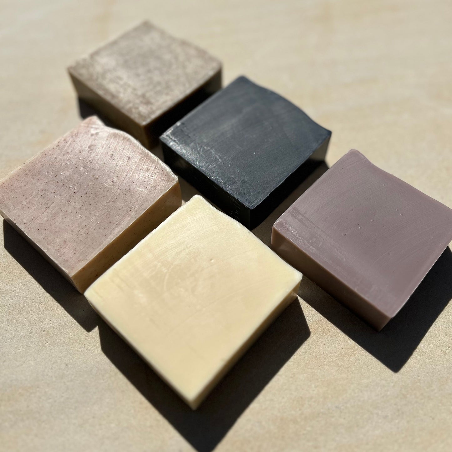 Five square bars of soap in different colours arranged on a beige surface