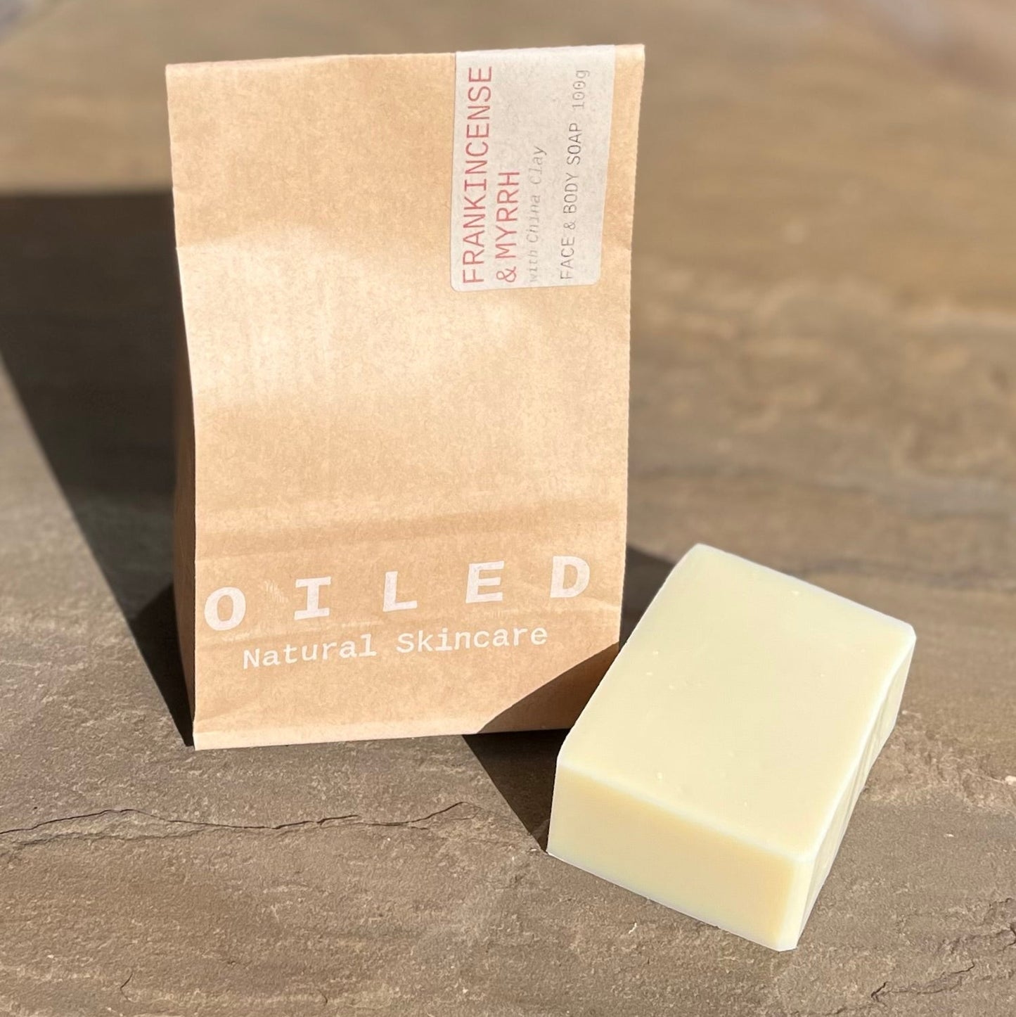 Bar of soap next to its brown paper bag packaging.