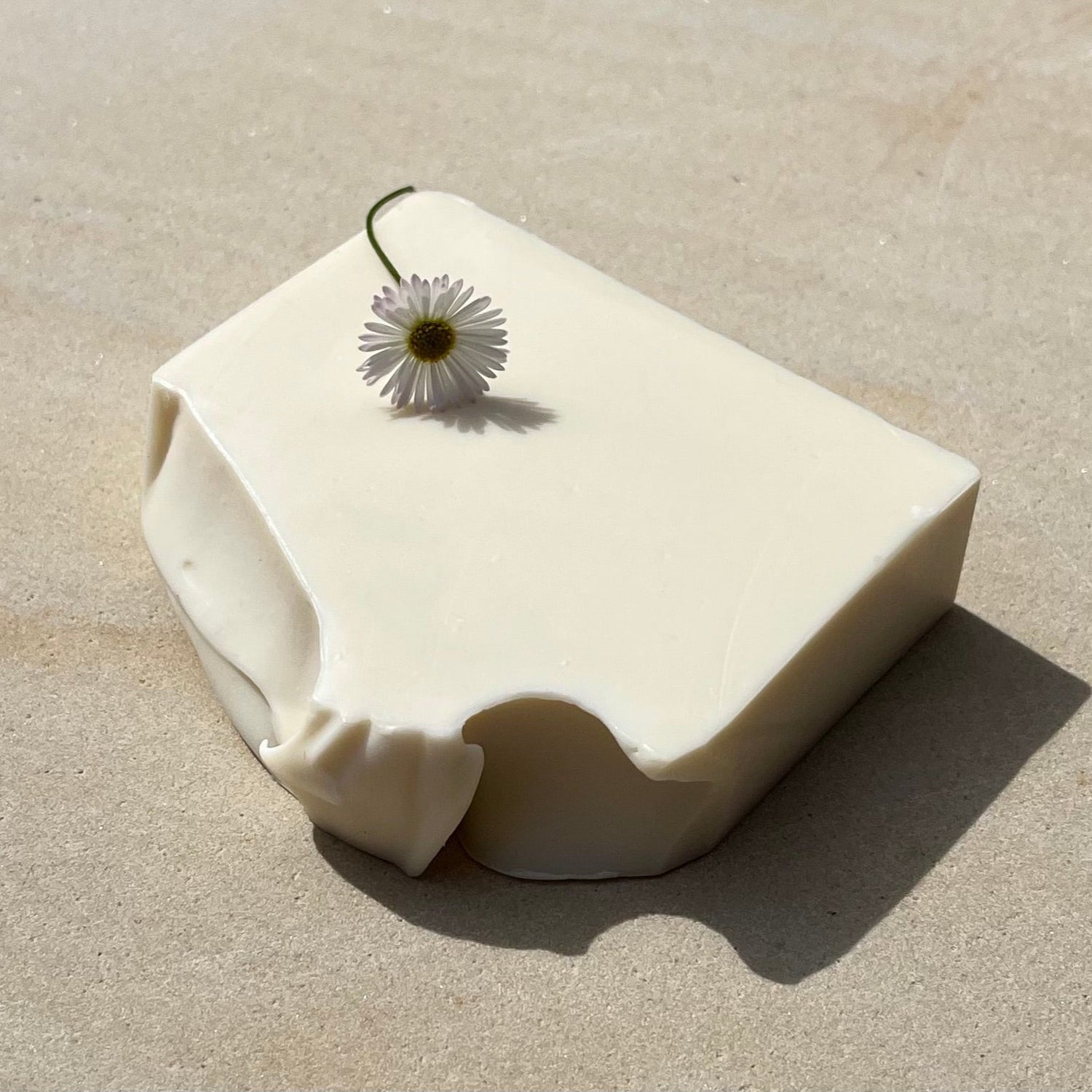 White and pink soap with geranium flower on top on a stone background.