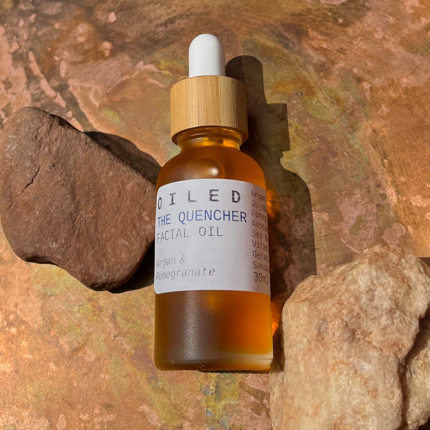 Facial oil dropper bottle labeled 'Oiled The Quencher' on a stone background