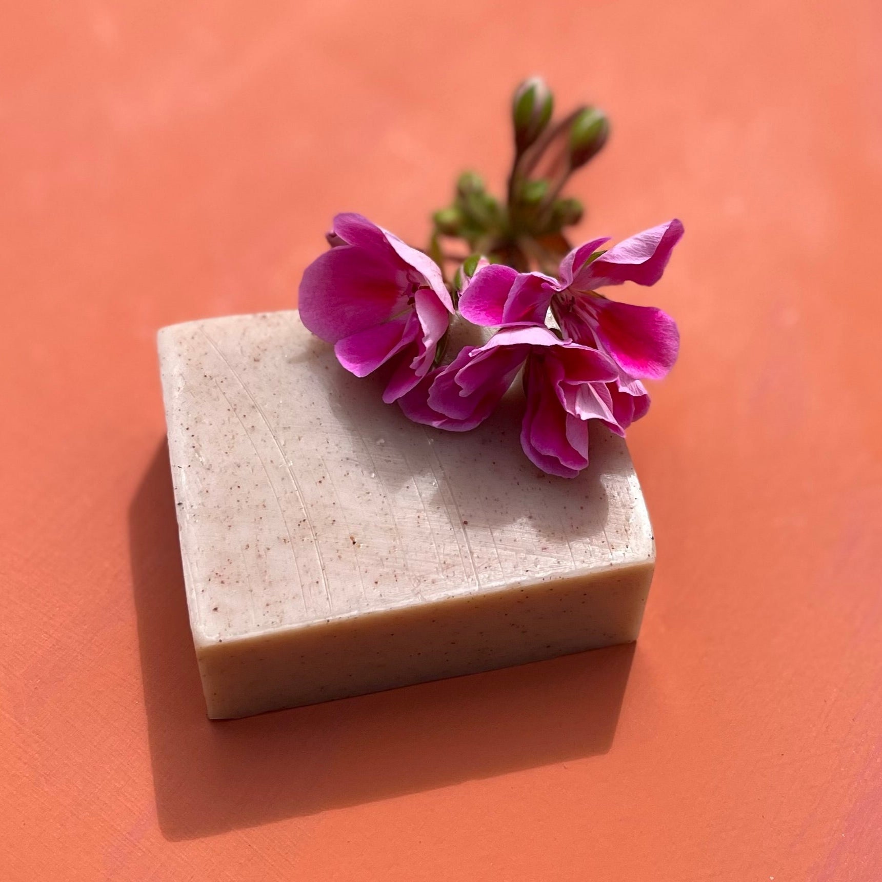 Bar of soap with a pink geranium flower on an orange background