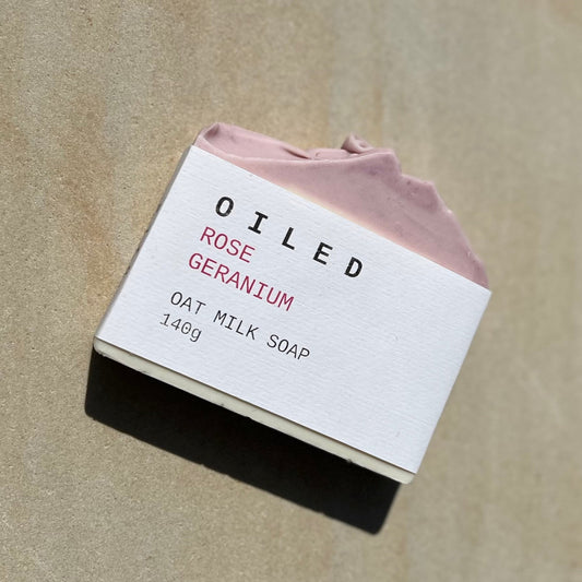 Bar of  Rose Geranium soap with a pink top and white label on a beige background