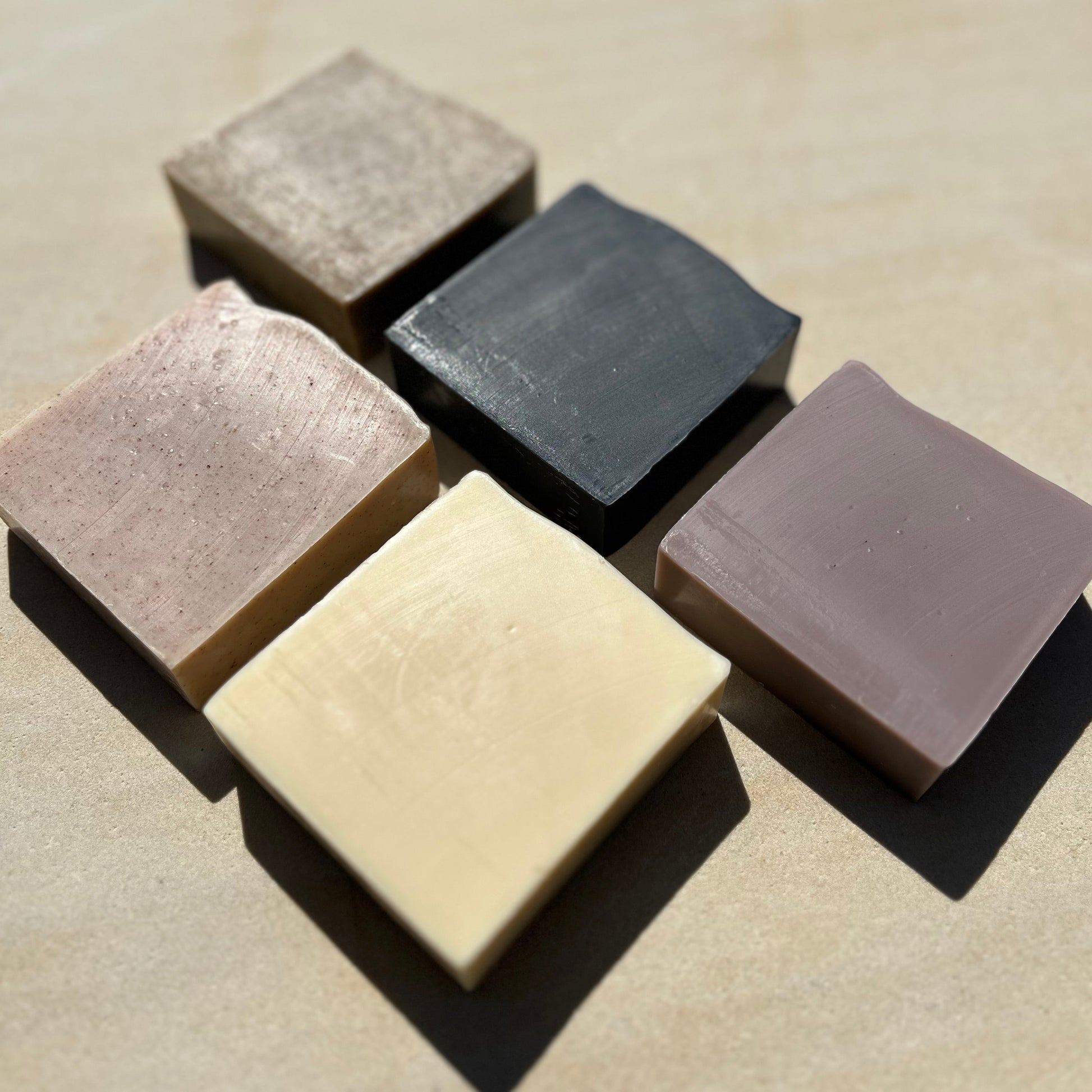 Five square bars of soap in different colours arranged on a beige surface