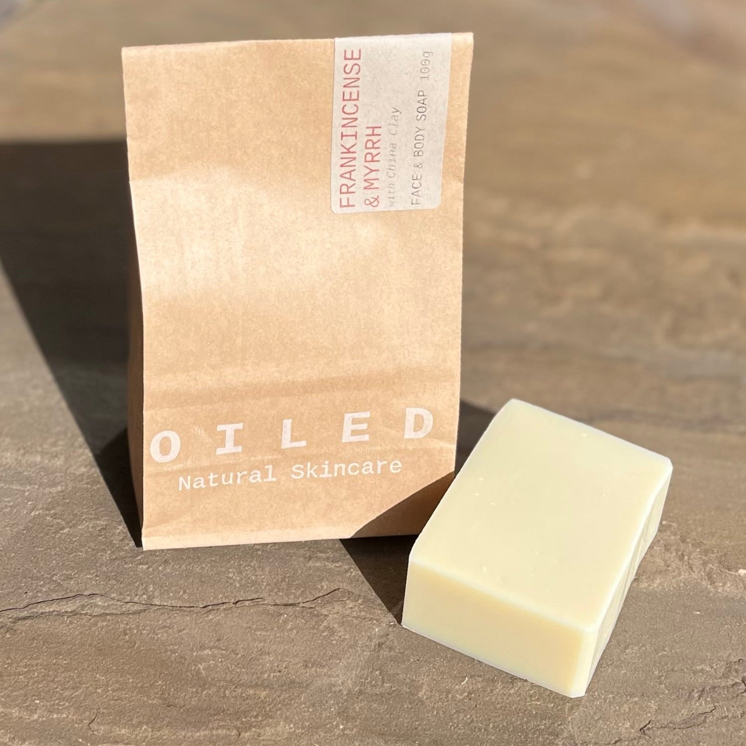 Bar of soap next to its brown paper bag packaging.