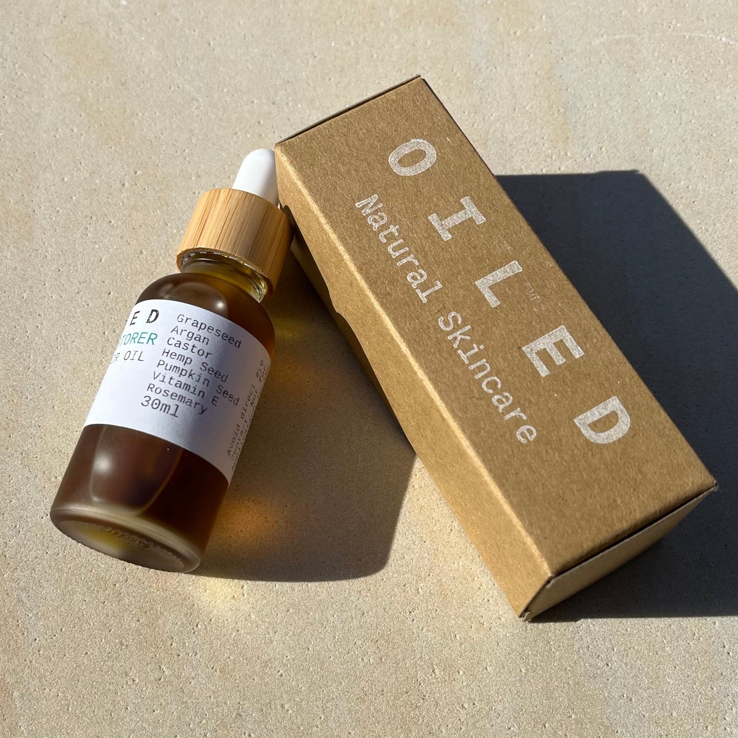 Skincare dropper bottle with a 'Oiled' branded box on a neutral background